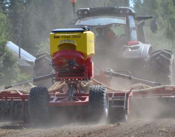 Tomu lentää pellon yllä, kun traktori vetää kylvökonetta perässään.