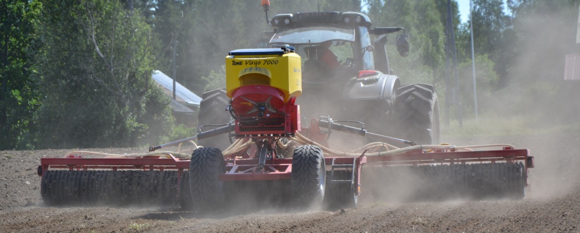 Tomu lentää pellon yllä, kun traktori vetää kylvökonetta perässään.